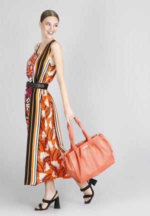 Buntes, florales Maxikleid mit vertikalen Streifen, tailliert mit einem schwarzen Gürtel. Das Model trägt eine korallenfarbene Handtasche und schwarze Absatzsandalen.