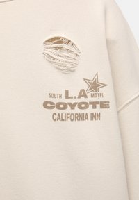 Tissu beige avec un trou usé et un texte marron indiquant South L.A Motel Coyote California Inn avec un graphisme d'étoile.