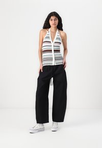 Striped sleeveless top in pastel colors with a V-neck and button closure, paired with loose black pants and white sneakers.