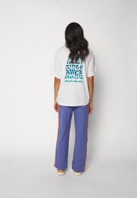 Witte oversized t-shirt met blauwe tekst "GIRLS RULE." Gecombineerd met paarse broek met oranje zijstrepen. Zacht katoenmateriaal, comfortabele pasvorm.