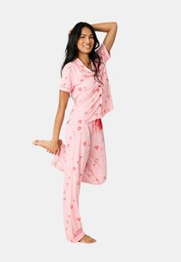 Roze katoenen pyjama set met een korte mouw top met knoopsluiting en bijpassende broek. Het ontwerp bevat harten en bloemenpatronen.