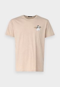 Lys beige bomull t-skjorte med korte ermer. Har et lite svart og hvitt grafisk motiv av en figur med vinger på venstre brystområde.