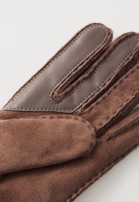 Brune hansker laget av semsket skinn og lær, med et sydd lærpanel og synlige sømmer. Designet med fire fingre og en myk tekstur.