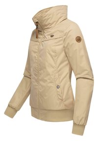Beige geïsoleerde jas met een hoge kraag, rits aan de voorkant en geribde manchetten. Heeft een zijzak en een merkembleem op de arm.