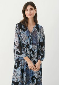 Pitkähiha, musta mekko, jossa on sinisiä ja valkoisia paisley-kuvioita, V-mallinen kaula-aukko ja napit, valmistettu kevyestä kankaasta.