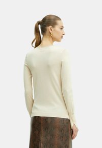 Top a maniche lunghe aderente color crema con texture a coste, dotato di dettagli con bottoni sui polsini e scollatura rotonda.