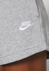 Pantaloni corti grigi in cotone con una texture liscia, caratterizzati da un logo Nike ricamato di colore bianco sul lato sinistro in basso e orlo cucito.