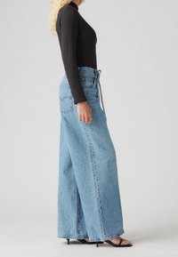 Ljusblå, vida denimjeans med hög midja och knytning, i kombination med en figurnära svart långärmad topp och svarta öppna klackar.