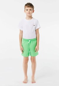 Witte t-shirt met roze logo en groene zwembroek. Elastische tailleband met trekkoord, gladde textuur en eenvoudig ontwerp.