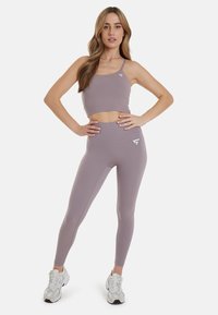 Light purple sports bra and leggings made from stretchy fabric, featuring a logo on the chest and hip, paired with white athletic shoes.