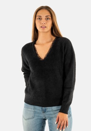 Maglione nero a scollatura a V con una lavorazione a maglia testurizzata, caratterizzato da un bordo in pizzo attorno allo scollo. Maniche lunghe e vestibilità comoda. Abbinato a jeans blu.