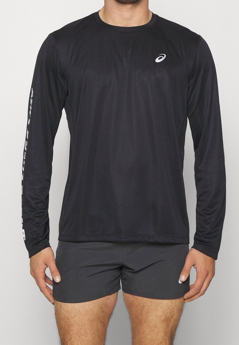 Langärmliges, schwarzes Sportshirt aus leichtem Material, mit Rundhalsausschnitt und Logo auf der Brust und dem Ärmel. Kombiniert mit grauen Shorts.