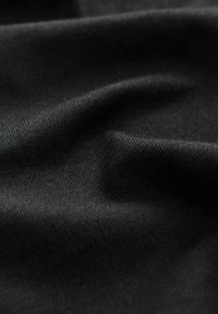 Gros plan sur un tissu noir lisse montrant une texture fine tissée et de doux plis.