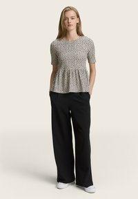 Blusentop mit Blumenmuster und kurzen Ärmeln in Schwarz-Weiß-Punkten; kombiniert mit lockeren schwarzen Hosen und weißen Sneakers.