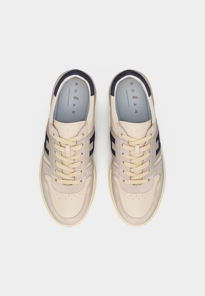 Ζευγάρι μπεζ και ναυτικά αθλητικά παπούτσια Hogan με κορδόνια και σουέντ λεπτομέρειες, φωτογραφημένα από ψηλά σε λευκό φόντο.