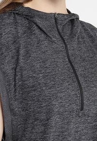 Grå sportig ärmlös topp med huva, som har en kvartsglidlås och ett strukturerat tyg. Designen kännetecknas av sidospjäll.