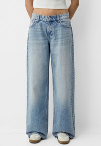 Jeans largi de un albastru deschis, cu un aspect decolorat, având bucle pentru curea, cinci buzunare și o închidere cu nasture. Finisate cu un tiv brut și ușoare distrugeri.