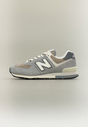 Baskets New Balance grises et beiges avec logo blanc "N", panneaux en mesh et en suède, semelle noire sur fond neutre, vue latérale.