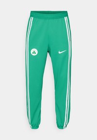Green athletic pants with white side stripes, featuring a Celtics logo patch and a Nike logo on the front, elastic waistband, and cuffed ankles.