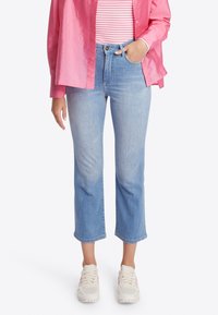 Jeans cortos de denim en azul claro, con cintura alta y diseño de pierna recta, combinados con una camisa de botones rosa y zapatillas blancas.