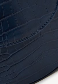 Pelle blu navy con texture a coccodrillo, caratterizzata da una finitura liscia e cuciture a contrasto lungo il bordo.