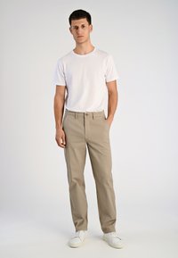 Beige katoenen broek met een rechte pasvorm, voorzien van een knoopsluiting, zijzakken en een eenvoudige witte t-shirt met ronde hals. Witte sneakers maken de look compleet.
