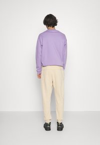 Violetti puuvillainen collegepaita yhdistettynä kermaisiin, rentoihin collegehousuihin. Jalkineissa on musta, teksturoitu malli, jossa on vihreitä yksityiskohtia.