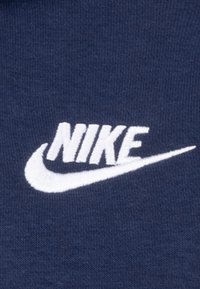 Tissu bleu marine avec une surface texturée arborant un logo "NIKE" blanc brodé et un design de swoosh. Le logo est affiché de manière proéminente.