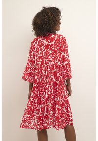 Robe florale rouge et blanche avec un design à volants, manches 3/4 et tissu fluide. Présente un col rond et une coupe décontractée.