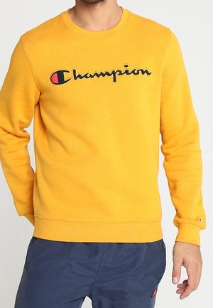 Felpa gialla in misto cotone, con collo a giro e polsini a coste. Presenta un ampio logo nero "Champion" sul petto.