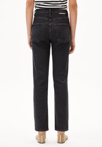 Jean noir taille haute avec jambes droites, comportant deux poches arrière et des détails de couture. Présenté de dos, avec une chemise rayée dépassant au-dessus.