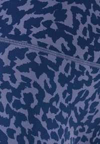 Primo piano di un tessuto con stampa animale blu navy e grigio, con una cucitura orizzontale visibile e dettagli di cucitura a coste.