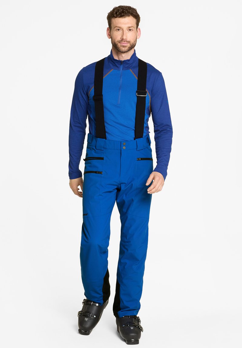 Pantalons de ski isolés bleus avec des bretelles noires réglables, poches latérales zippées, et associés à un haut à manches longues bleu assorti.