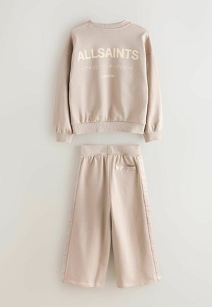 Set format dintr-un pulover ușor bej și pantaloni scurți asortați, realizat dintr-un material texturat, cu manșete rib și buzunar în partea din spate a pantalonilor scurți.