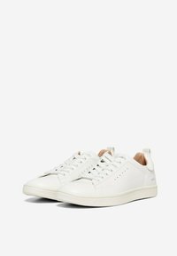 Baskets blanches en cuir lisse avec un bout arrondi, un design à lacets et des trous de ventilation minimaux. Présentent une doublure intérieure beige et un branding subtil.