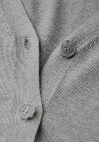 Cardigan en tricot gris présentant un tissu texturé, deux boutons ronds gris clair et un boutonnière visible sur le devant.