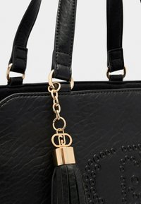 Borsa nera con texture, dotata di doppi manici, chain in oro e chiusura che regge un tassel in pelle nera sul lato anteriore.