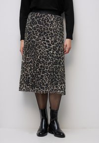 Midi sukně s leopardím potiskem a sklady v odstínech hnědé a černé. Obsahuje černý elastický pas a je kombinována s černými kotníkovými botami.