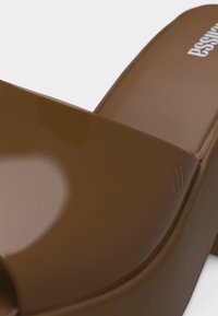 Κοντινή λήψη ενός καφέ γυαλιστερού σανδάλιου πλατφόρμας με φαρδιά λουρί και χοντρό τακούνι.