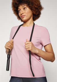 Short-sleeve pink athletic T-shirt with a smooth texture, held with a black jump rope. T-shirt features a crew neck and fitted design.