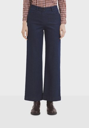 Wide-leg dark blue denim pants with a high waist, featuring front pockets and a button closure, paired with brown ankle boots.