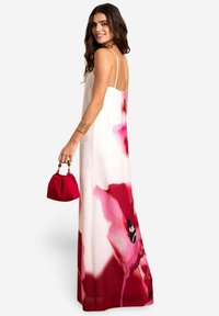 Maxikleid aus leichtem Stoff, mit weißem Grund und großen rosa Blumenmustern. Es hat dünne Träger und eine luftig-leicht fallende Silhouette.