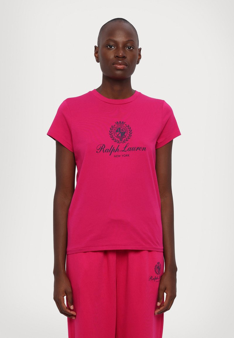 T-shirt de algodão rosa com decote redondo e mangas curtas, adornada com uma impressão de logotipo preto no centro, combinada com calças a condizer.