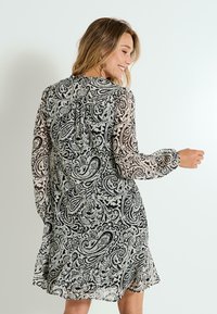 Vestido de patrón paisley en blanco y negro con mangas largas y transparentes, detalle en la parte trasera con fruncido y dobladillo acampanado. Tejido ligero y fluido.