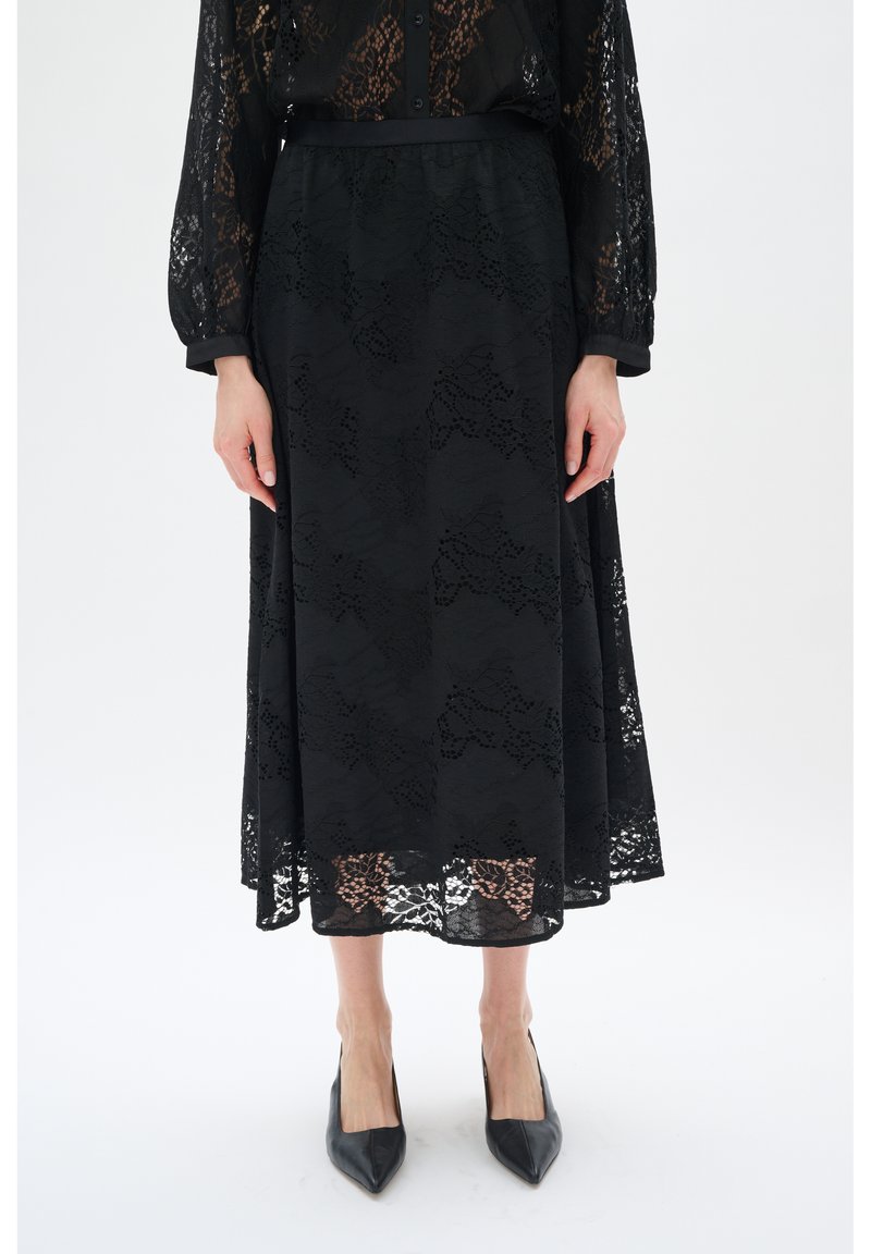 Schwarzer Spitzenrock mit fließendem Design, aufwendigem Blumenmuster und semi-transparenter Textur. Kombiniert mit schwarzen spitzen High Heels.