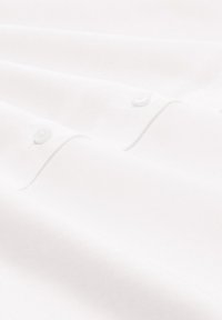 Weiße Baumwollhemdstoffe mit einer glatten Textur, die zwei sichtbare Knöpfe und dezente Stichdetails aufweisen.