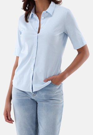 Jasnoniebieska koszula na krótki rękaw z kołnierzykiem, wykonana z gładkiej tkaniny. Posiada luźny krój i subtelny połysk. Noszona z jasnymi dżinsami.