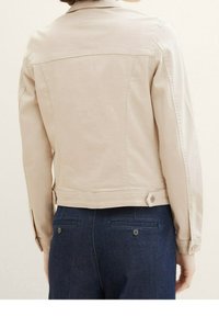 Beige denim jacket with a slightly fitted shape and a standard collar. Features button closures and stitching details on the back.