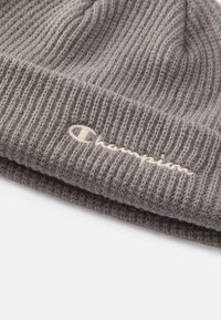 Grå ribbestrikket lue laget av mykt stoff, med en brettet kant med brodert tekstlogo i kremfarge.