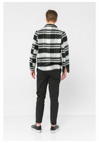 Svart och vit rutigt ulljacka med avslappnad passform, knappstängning och ryggslits. Matchad med svarta byxor och texturerade skor.